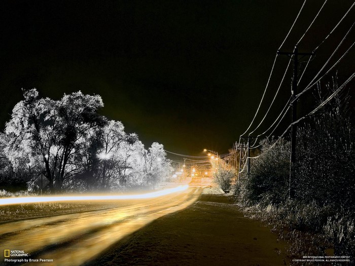 Night road with light trails and ice-covered trees