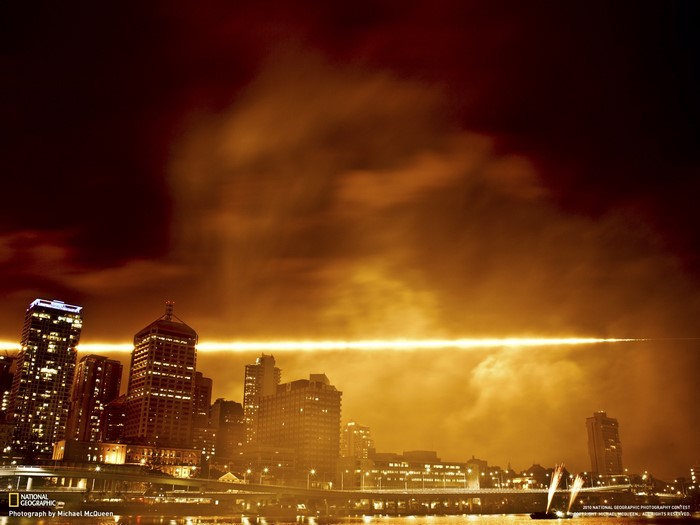 Cityscape at night with a bright light beam across the sky