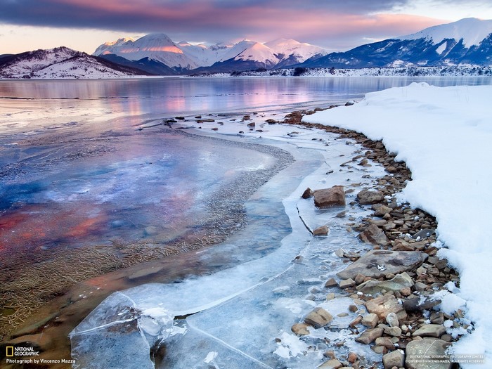 Frozen lake with snow-capped mountains at sunrise