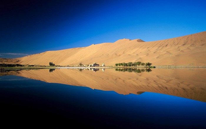 Desert oasis with crescent lake and sand dunes reflection