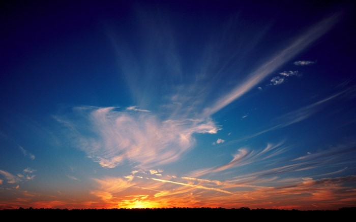 Sunset with wispy clouds over a silhouetted horizon