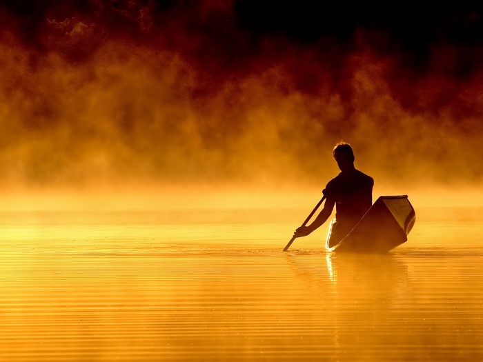 Man in canoe on misty lake at sunrise