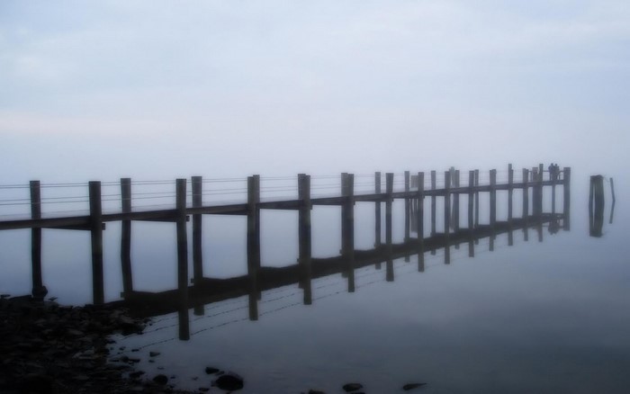 Pier in fog over the ocean with reflections