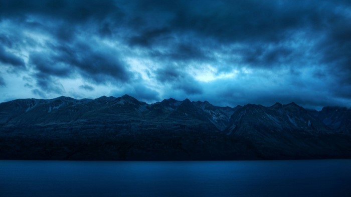 Dark Mountain Range Overlooking a Calm Lake Under Stormy Skies