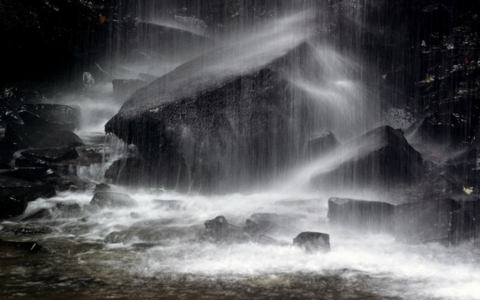 Monochrome waterfall cascading over dark rocks