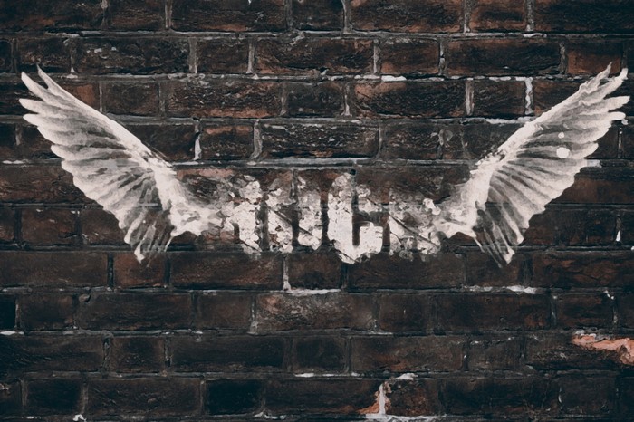 Graffiti of wings and text on a brick wall