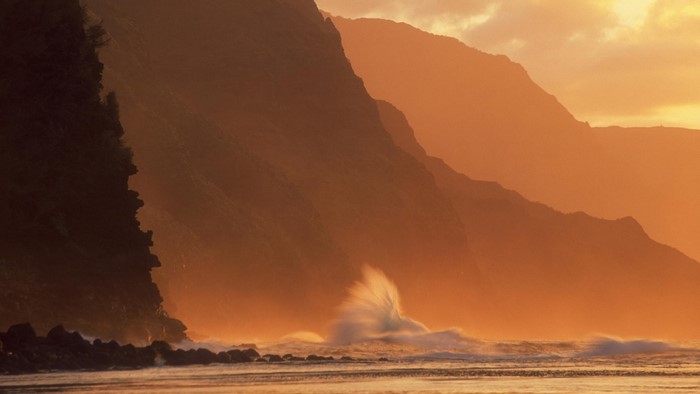 Orange sunset over mountains and ocean waves