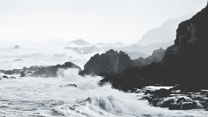 Monochrome waves crashing on rocky coast with misty mountains