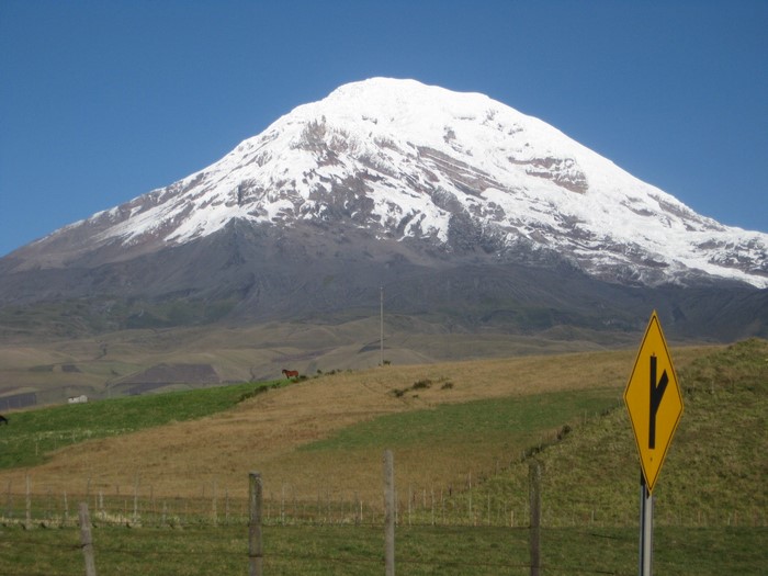 Snow-capped mountain with horses and road sign