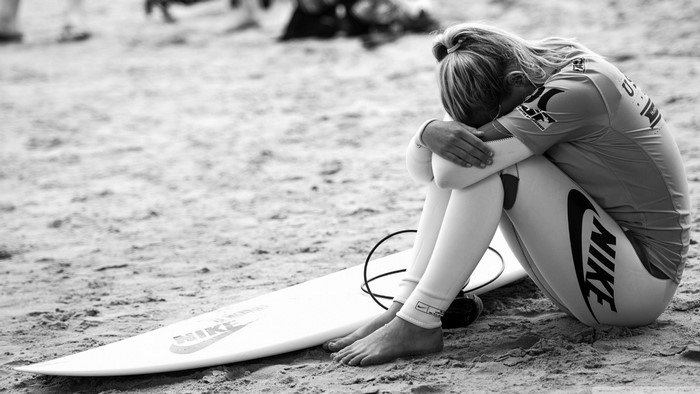Surfer in wetsuit sitting on beach with surfboard