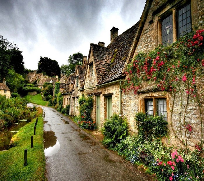 Stone cottages with blooming flowers along a wet road