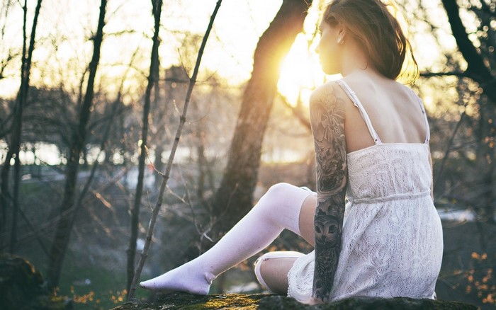 Woman with tattoos sitting in a forest at sunset