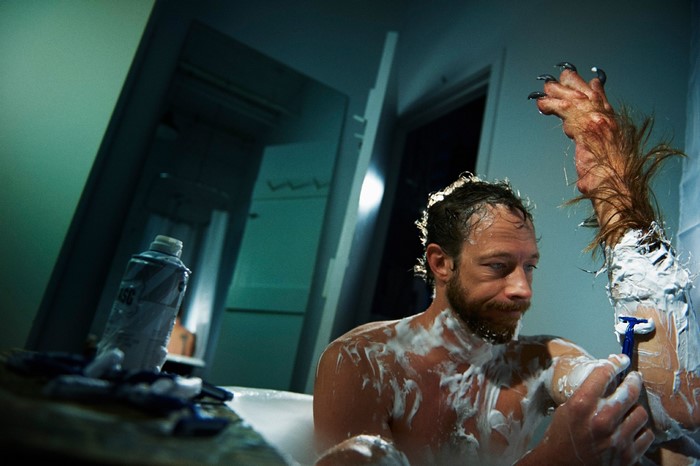 Man with werewolf arm shaving in bathtub