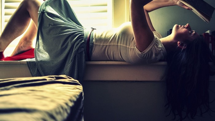 Woman lying on windowsill reading a book