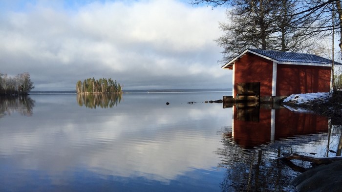 Red boathouse on a calm lake with island reflection