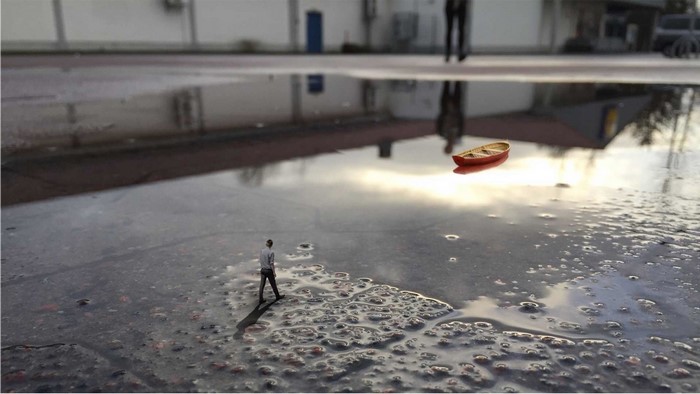 Miniature man and boat in puddle reflection