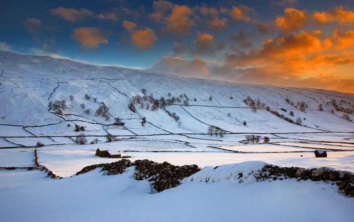 Snowy landscape with stone walls and hills at sunset