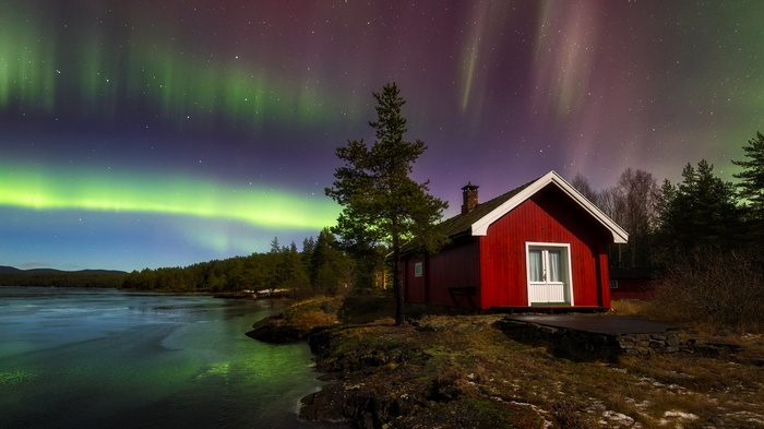Red cabin under the Aurora Borealis by a lake