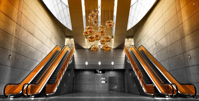 Modern escalator hall with orange accents and spherical chandeliers