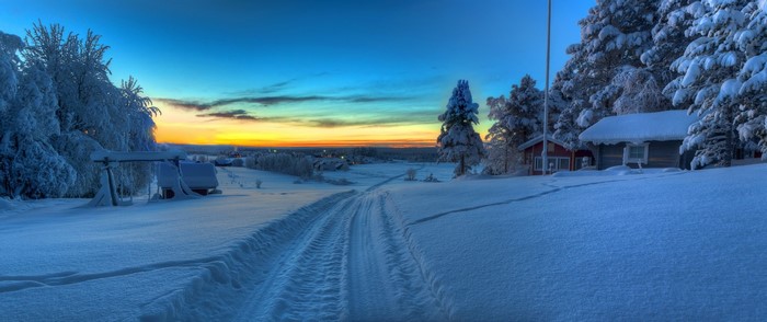 Snowy landscape with a track leading to a small village at sunset