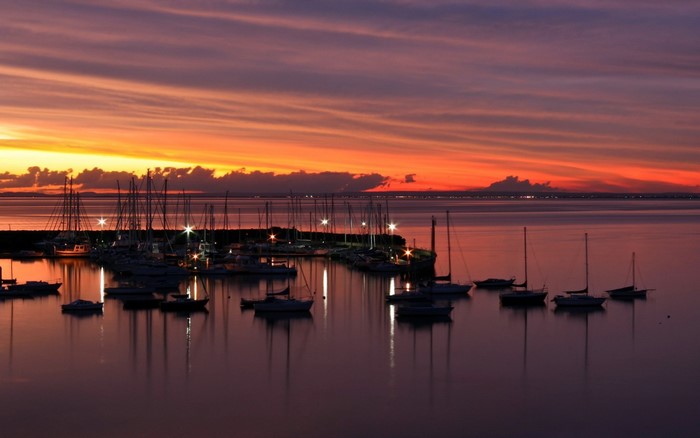 Boats docked at a marina during a colorful sunset over the water