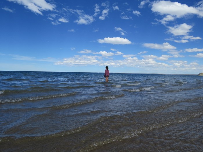 A girl stands in the ocean with waves and clouds