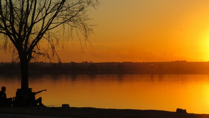 Sunset over a lake with people by a tree