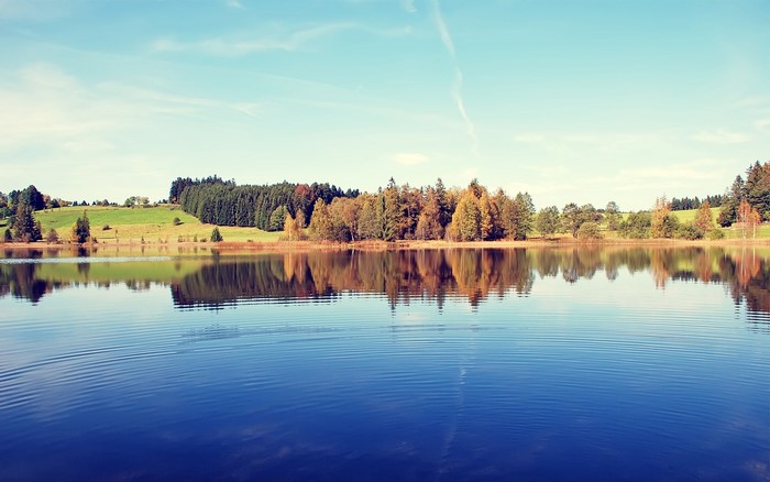 Lake with reflections of trees and hills under a blue sky