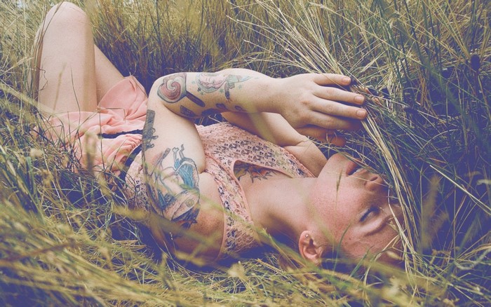 Woman with tattoos lying in grass