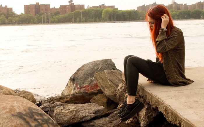 Redhead woman sitting on rocks by the water