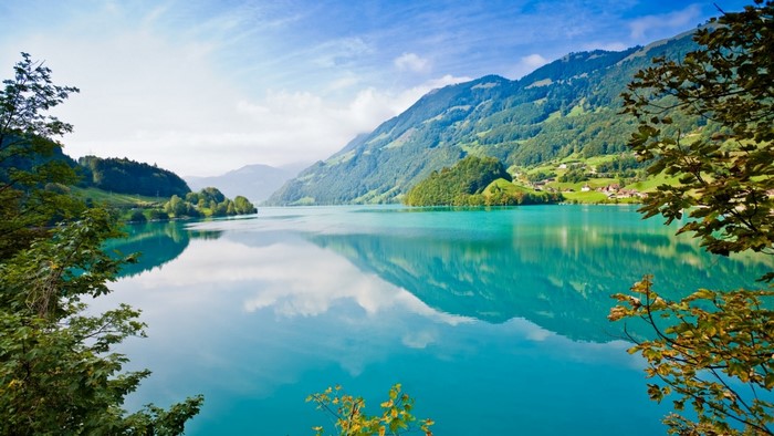 Turquoise lake reflecting mountains and trees under a blue sky
