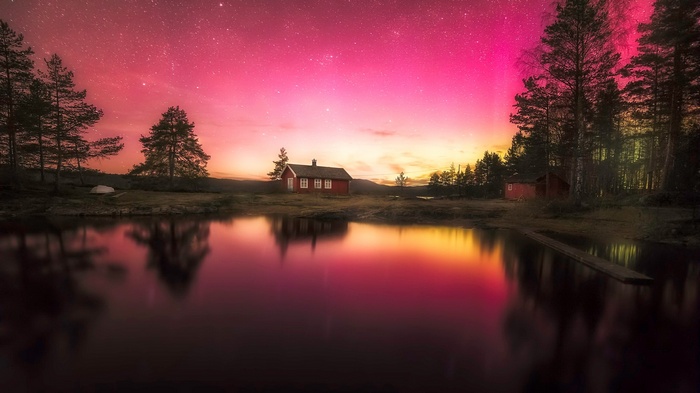 Red cabin by lake under aurora borealis
