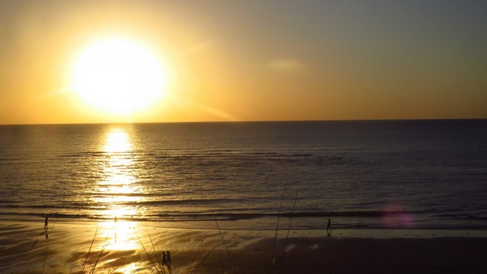 Sunset over the ocean with people on the beach