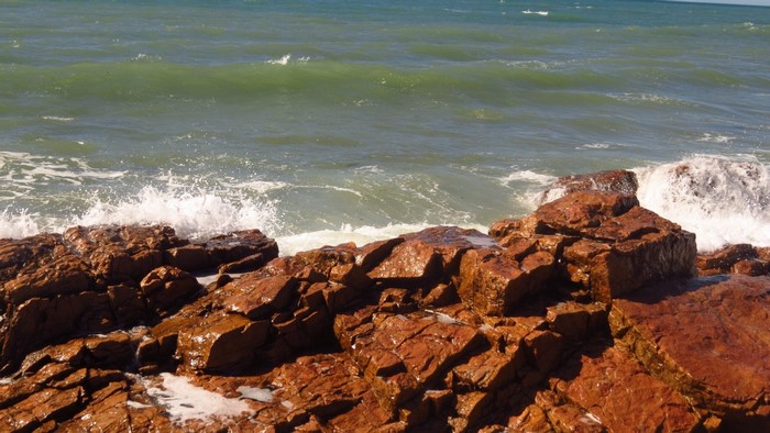 Waves crashing on reddish-brown rocks by the sea
