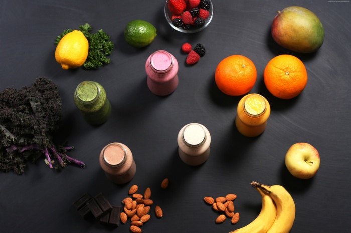 Assortment of fruits, smoothies, chocolate, and nuts on a dark surface