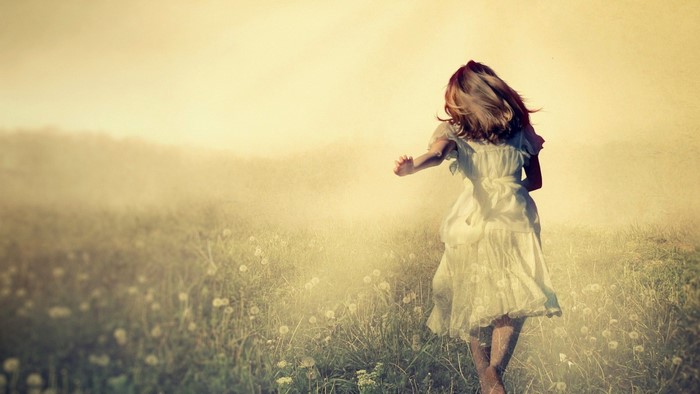 Girl in white dress running through a field of flowers