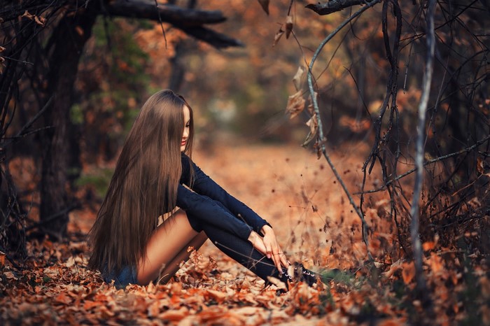 Woman with long brown hair sitting in autumn forest