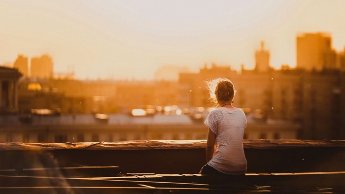 Woman sitting on rooftop at sunset overlooking city