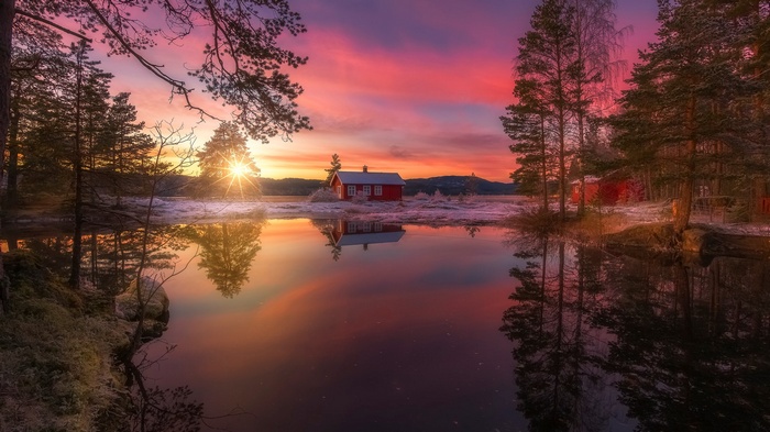 Red cabin by a lake at sunset with pine trees