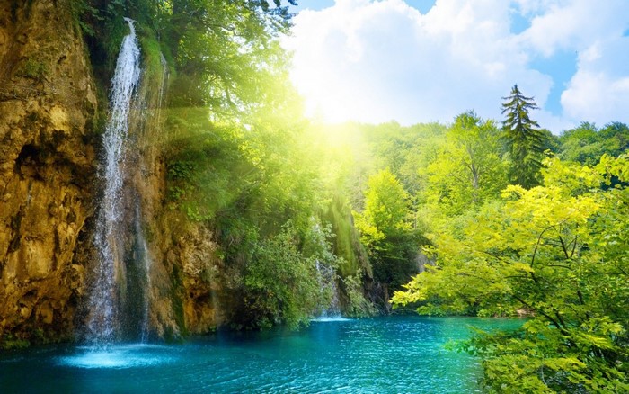 Waterfall in a sunlit forest with a turquoise lake