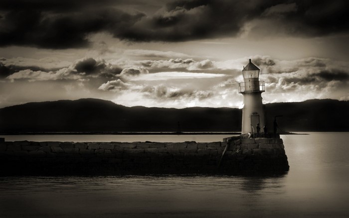 Monochrome lighthouse on a stone pier at dusk
