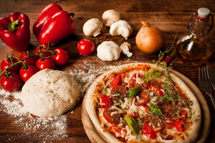 Pizza ingredients and a finished pizza on a wooden table