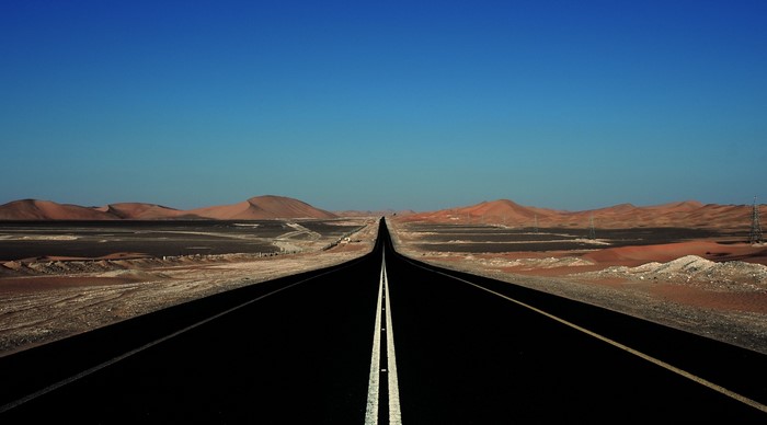 Desert highway with sand dunes under a clear blue sky