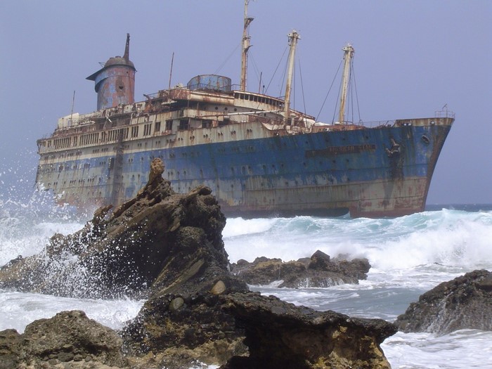 Abandoned ocean liner wreck on rocky coast with waves