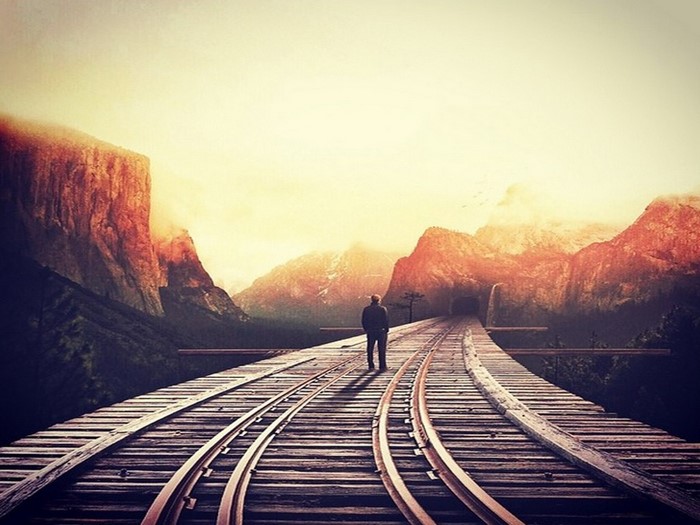 Man on train tracks in mountains at sunset