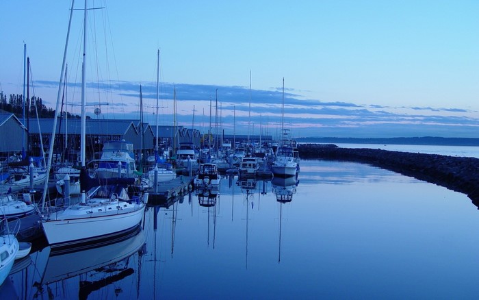 Boats docked in a harbor at dusk with reflections