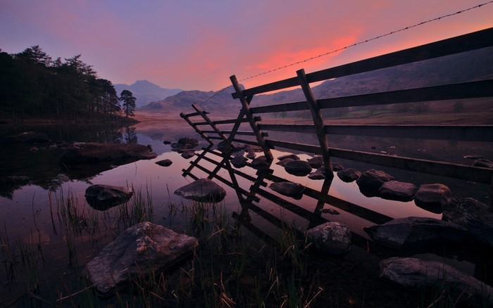 Wooden fence in lake at sunset with mountains