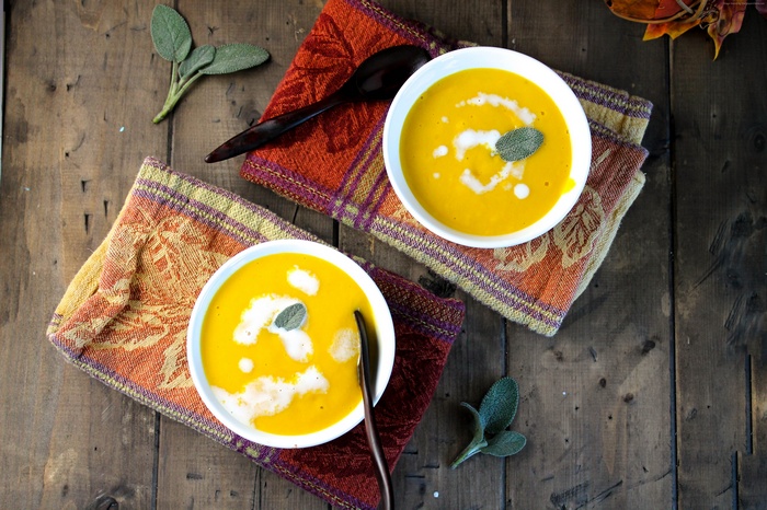 Two bowls of pumpkin puree soup with cream and sage