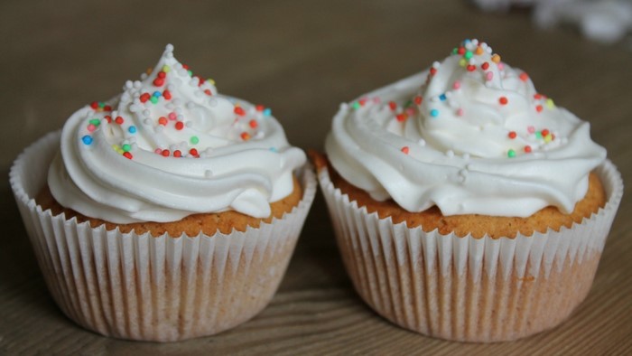 Two cupcakes with white icing and sprinkles