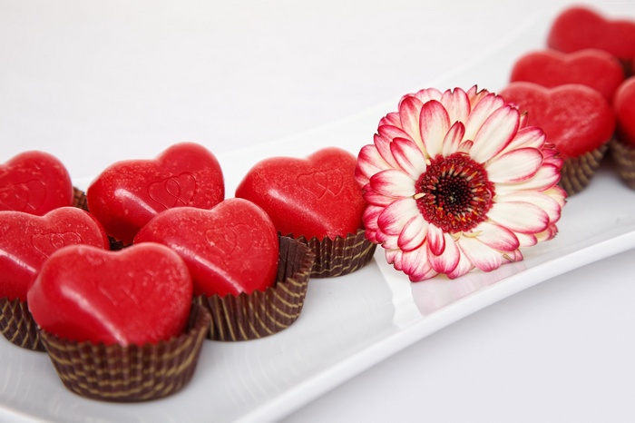 Red heart candies and a gerbera daisy on a white plate